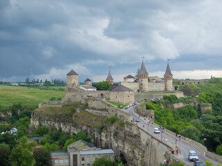 Fototapeta na wymiar Kamianets Podilsky fortress on cloudy summer day. Scenic summer view of ancient fortress castle in Khmelnytskyi Region, Ukraine. Medieval stone large castle fortress with spiers and defensive towers.