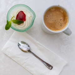 Dessert with whipped cream and cup of coffee, paper napkin, spoon on cotton fabric background.