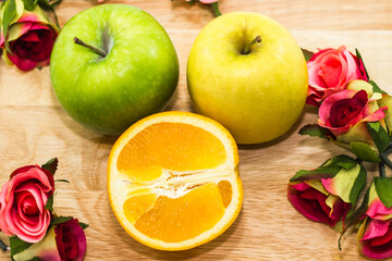 Apple and orange cut in half, put on a wooden cutting board with flowers around it.