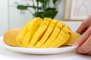 Hands holding a dish of fresh juicy sliced Mango from living room table