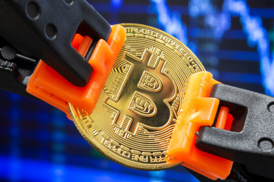 Representative bitcoin between plastic clamps in selective focus. The concept of suppressing bitcoin, stopping the rise. Cryptocurrency, stock market, blockchain, digital money concept.