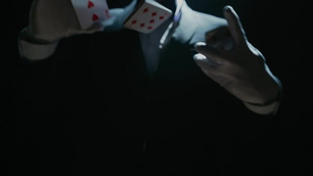 Close-up of a Suited Magician's Hands Performing Sleight of Hand Card Tricks. Cards fly and turn over in the air. Slow Motion. Background is Black.