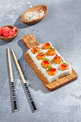 Maki roll with salmon and tobiko caviar on wooden board in contemporary composition. Sushi roll with chopsticks on concrete table. Maki sushi with salmon top in minimal style.