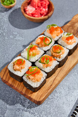 Maki roll with salmon tartare top and tobiko on wooden board in contemporary composition. Sushi roll with chopsticks on concrete table. Maki sushi in minimal style.