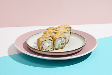 Tempura maki with shrimp on ceramic plate. Hot tempura sushi with shrimp, cucumber and cheese on coloured background. Japanese menu concept. Hot maki sushi in modern style.