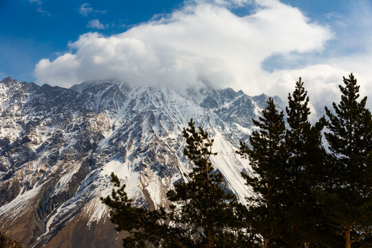 Scenic mountain landscape of snow-capped Greater Caucasus Range with rocky peaks covered with clouds against blue sky in early spring. Nature of Georgia
