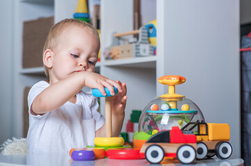 Handsome toddler boy playing with educational wooden and plastic toys in children's room..