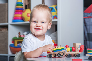 Handsome toddler boy playing with educational wooden and plastic toys in children's room..
