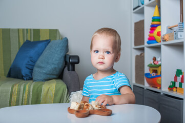 Toddler boy eats on his own at table at home..