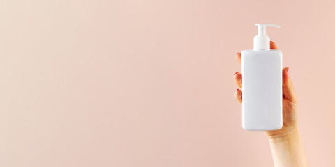 A mockup of a white dispenser with a cosmetic product in a woman's hand on a light pink background.