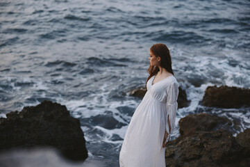 pretty woman with wet hair in wedding dress by the ocean rocks