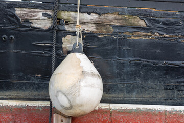 White buoy hanging from a weathered ship side. Cracked wood and paint.
