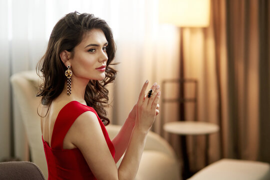 Closeup of a beautiful sensual brunette woman in red dress with healthy curly hair and glamour makeup, shows jewelry.