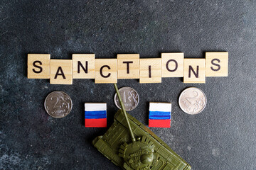 Sanctions against Russia concept. Toy tank, rubles and the inscription Sanctions on a dark background. War conflict in Ukraine, default, economic and monetary crisis in Russia.