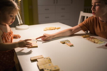 children play board game of dominoes at home in evening by light of table lamp