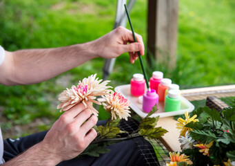 Closeup of a male artist's hands painting silk flowers outdoors