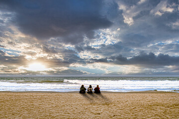 3 Frauen sithen am bewölkten Strand bei Sonnenuntergang