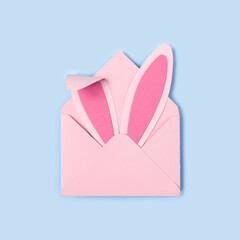Happy Easter. Bunny rabbit ears made of pink paper in pink envelope on blue background. Easter greeting card with envelope. Happy Easter minimal concept with copy space. Square format, Flat lay