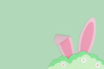 Happy Easter. Pink Bunny rabbit ears hide in grass made of green paper on green background. Easter greeting card template. Creative easter minimal concept with copy space. Flat lay