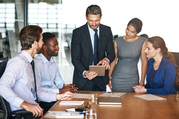 Running the numbers past his team. Shot of a group of corporate colleagues talking together over a digital tablet in an office.