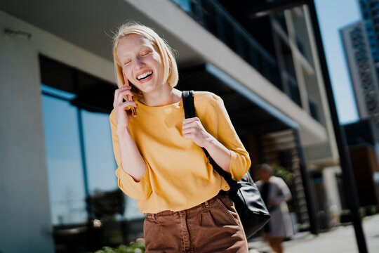 Happy girl walking on the street using the phone. Beautiful blonde girl talking to the smartphone..