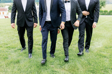 The groom and his friends walk on the green lawn, dressed in beautiful stylish suits. Large mans group of business executives approaching walking towards the camera led by a man