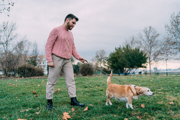 Young man walking his dog on a leash in park on grass