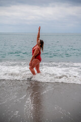 Woman in a bathing suit at the sea. A fat young woman in a red swimsuit enters the water during the surf