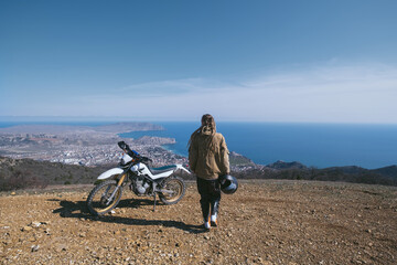 Obraz na płótnie Canvas Female rider relaxing in enduro offroad motorcycle travel on mountain top, beautiful sea shore and mountains landscape on background