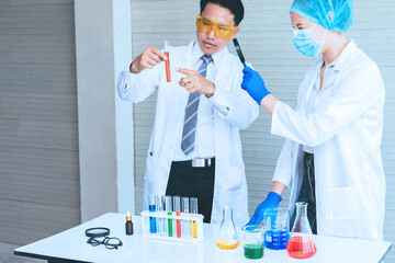 Scientist team in uniform holding beaker and test tube have chemical liquid for testing chemical reaction.