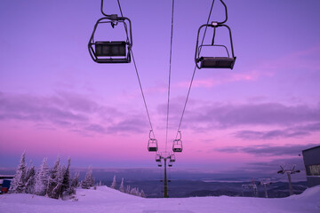 Ski lift in snowfall in mountains ski resort. Pink purple winter sunset view, landscape with chairlifts  and mountain skyline