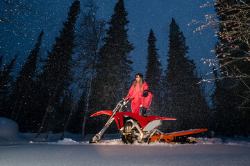 Woman standing on snowbike in winter forest, night portrait in flash light