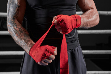 Red bandages on the hands of a kickboxer against the background of the ropes of the ring. The...