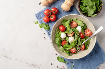 Fresh salad with arugula, cherry tomatoes, mozzarella cheese and hard cheese on white wooden background. Top view
