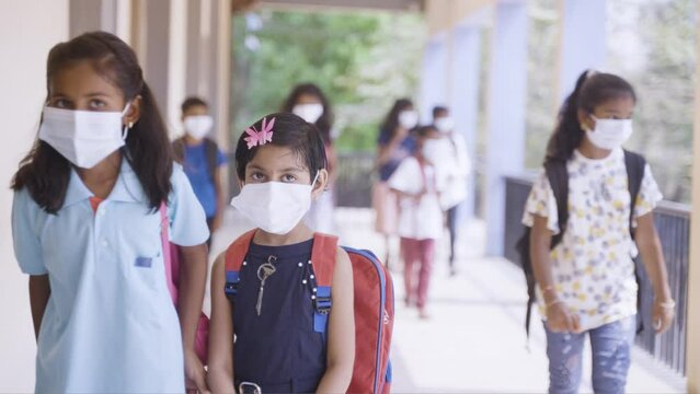 rack focus shot, Group of kids with medical face mask going to classroom at school corridor after coronavirus or covid-19 pandemic - concept of back to school, safety measures and protection.