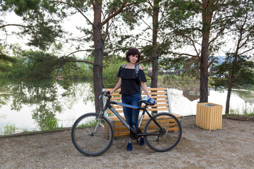 Fototapeta premium An adult female tourist with a backpack on her back riverbank with a bicycle.