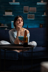 Depressed woman watching sad movie on television and eating popcorn, doing leisure activity at home. Anxious person in solitude suffering and looking at film on TV channel program.