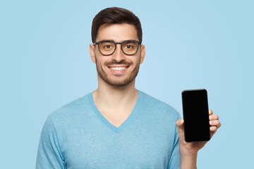 Young man in blue t-shirt and glasses holding blank screen phone in vertical position