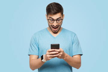 Young man holding phone in hands, looking at screen with excited wow face