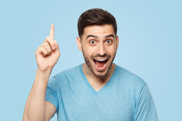 Young excited man in blue t-shirt, pointing upwards with finger, having great idea