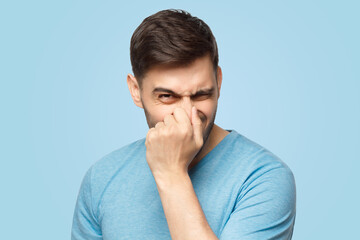 Young man holding his nose as if smelling something rotten and stinky