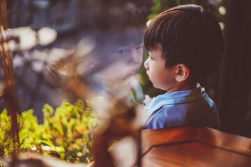 Kid looking out window. Adorable little caucasian kid boy stand still near window glass and looking...