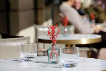 Street cafe, decorations in vase and two empty glasses on table outdoor. Romantic dinner in spring or summer city, elegant setting
