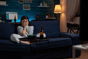 Terrified woman watching scary movie and covering eyes, feeling afraid in front of television screen. Young person being anxious to watch horror film alone in living room, leisure activity.