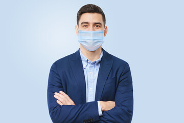 Young businessman in medical mask stands with crossed arms