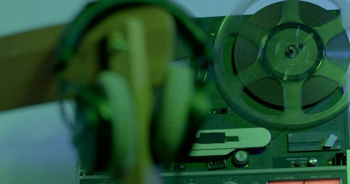 The movement of reels of tape on a tape recorder in green light. Using an old recorder to record and listen to audio. Headphones on the stele in bokeh.