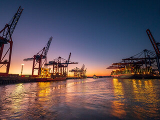Fototapeta na wymiar Hamburg industrial city shape during sunset with stunning orange light and silhouette machines