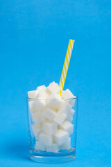 Glass with refined sugar cubes and a drinking tube on a blue background.