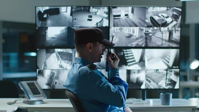 Security guard talking on walkie talkie while looking at cctv camera footage on multiple computer screen