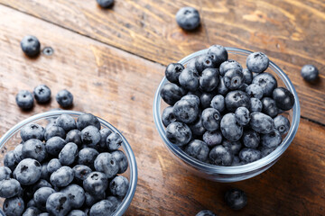 Freshly picked blueberries in a glass bowl on a wooden background. Healthy food and nutrition concept.